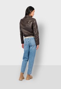 Veste cropped en cuir marron avec taille élastique, associée à un jean taille haute bleu clair et des bottes cheville beige. Vue arrière montrée.