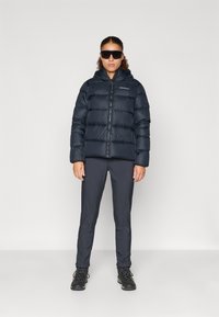 Puhvis, tume sinine jakk kapuutsiga, esine tõmblukk ja elastsed varrukad, koos tumedate hallide spordipükste ja mustade matkasaabastega.