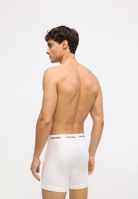 Bijele pamučne bokserice s mekim elastičnim pojasom na kojem se nalazi crni Calvin Klein logo. Kroj je uskog oblika s glatkom teksturom.