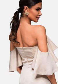 Robe beige à épaules dénudées avec des manches à volants fluides et un corsage ajusté. Comporte une fermeture éclair dissimulée au dos, texture lisse.