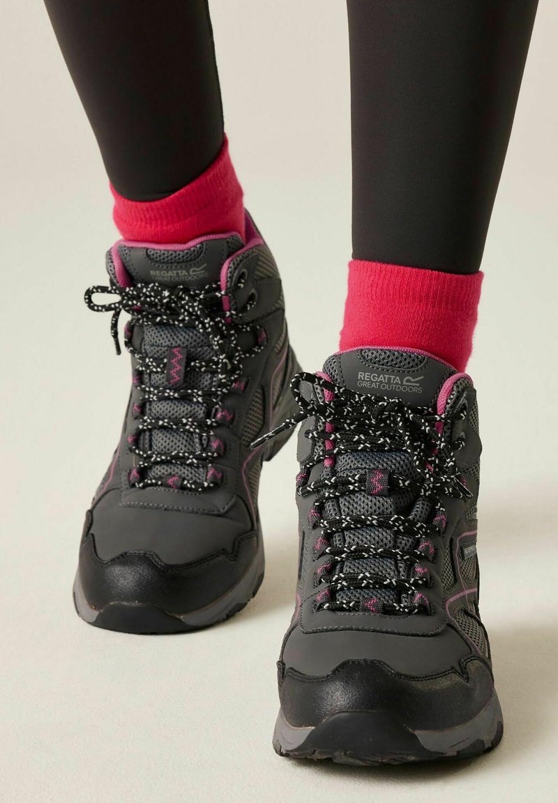 Grey and pink hiking boots with black and white laces worn with bright pink socks and black leggings on a light background.