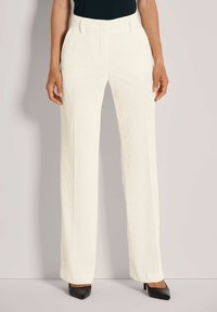 Witte fluweelachtige wijde broek met gestructureerde strepen, voorzien van een aansluitende taille en discrete zijzakken, gecombineerd met zwarte hoge hakken.