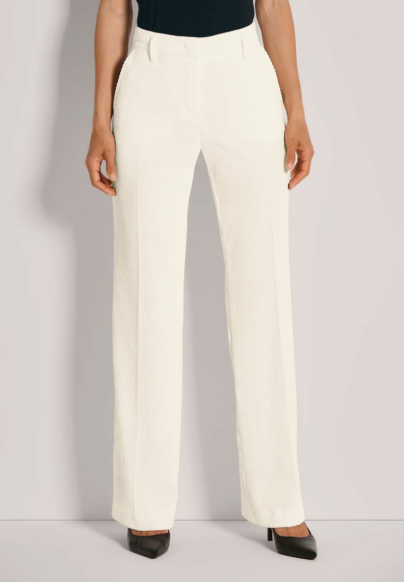 Witte fluweelachtige wijde broek met gestructureerde strepen, voorzien van een aansluitende taille en discrete zijzakken, gecombineerd met zwarte hoge hakken.