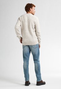Lichtbeige gestructureerde trui met een gebreid patroon, gedragen met lichtblauwe jeans en brown boots. Uitzicht van achteraf, toont het ontwerp en de pasvorm.