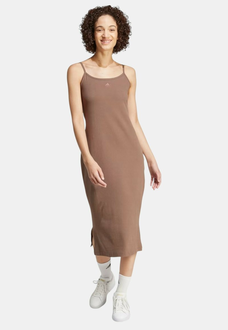 Abito tank marrone a coste con spalline sottili e spacchi laterali, abbinato a sneakers bianche e calzini alti. Design semplice e lineare.