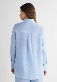  Lichtblauwe gestreepte shirt met een klassieke kraag, lange mouwen en knoopsluitingen aan de manchetten. Heeft een rugpand en een iets gebogen zoom.