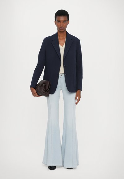 Navy blazer, cream v-neck top, light blue flared jeans, and woven dark bag. Smooth textures and contrasting colors create a cohesive look.