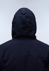 Granatowa kurtka z kapturem widziana od tyłu, charakteryzująca się gładką fakturą, regulowanym troczkiem na kapturze i minimalnym przeszyciem.