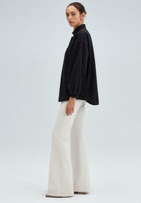 Zwarte corduroy oversized blouse met hoge kraag en ballonmouwen, gecombineerd met witte flared broeken met een soepele textuur en een minimalistisch ontwerp.