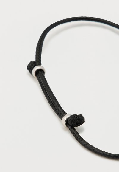 Čierny šnúrkový náhrdelník so zapletaným vzorom obsahuje dva strieborné kovové akcenty a detail s uzlom, čo vytvára kontrast textúr materiálov.
