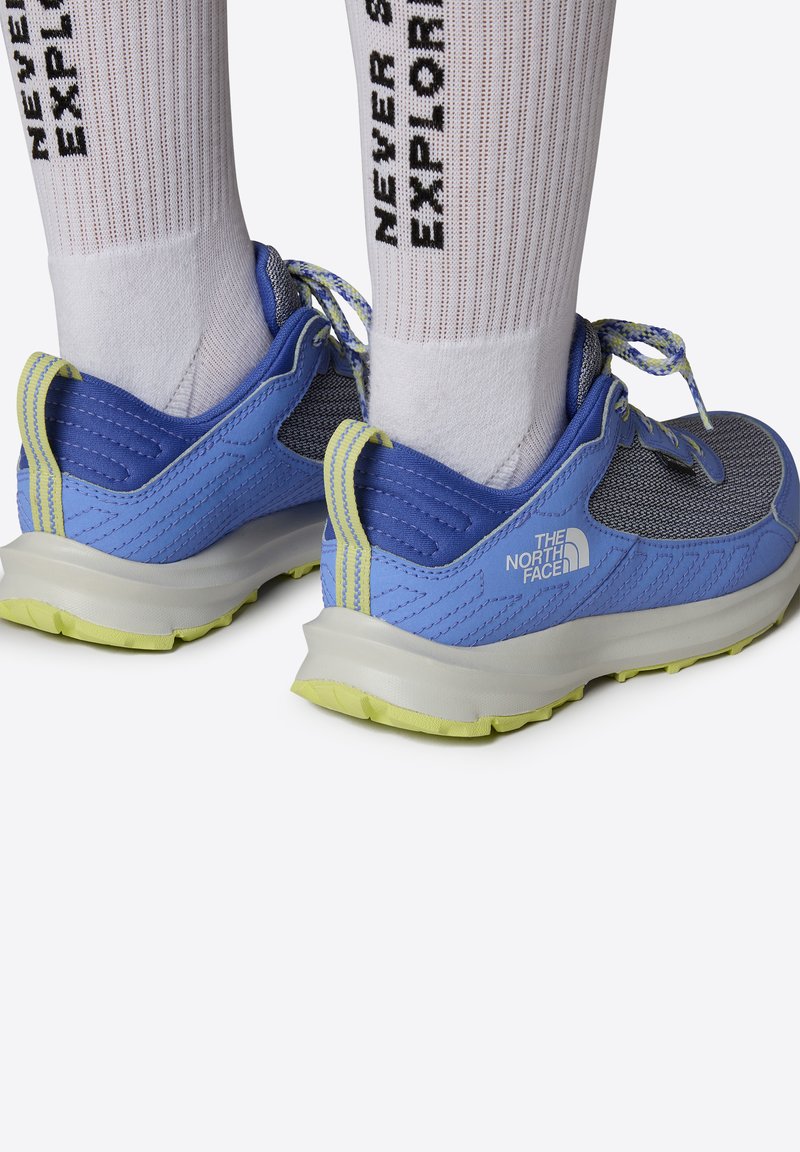 Zapatillas deportivas azules y grises con material de malla, talón reforzado y acentos amarillos. Suela de goma gruesa con patrón de agarre texturizado.