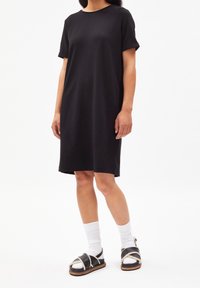Czarna bawełniana sukienka z krótkimi, zawiniętymi rękawami, sięgającym kolan dołem i luźnym krojem, w połączeniu z czarnymi sandałami i białymi skarpetkami.