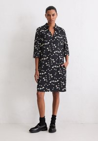 Czarna sukienka w biały kwiatowy wzór, z kołnierzykiem i rękawami do łokcia; posiada boczne kieszenie. Połączona z czarnymi mokasynami i skarpetkami.