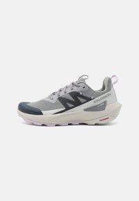 Chaussure de sport légère grise et violette avec tige en mesh respirant, lacets à motifs et semelle épaisse et rembourrée, arborant le logo Salomon sur le côté.
