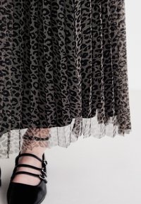 Plissierter Leopardenprint-Rock aus schwarzem und grauem Tüll mit einem durchsichtigen Saum. Schwarze spitze Ballerinas mit drei Riemen-Details sind sichtbar.