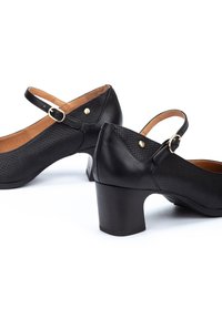 Talons en cuir noir avec des panneaux texturés et un bout rond. Présente une sangle avec une boucle dorée et un talon carré.