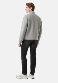 Lichtgrijs fleecejack met een hoge kraag, gecombineerd met donkere jeans en witte sneakers met beige en grijze accenten.