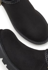 Črne semiš gležnjarje z pletenim trakom, okroglo konico in teksturirano podplatom z obrisom zigzag vzorca. Oblika ravnega pete.