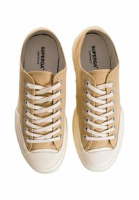Sneakers di tela beige con lacci bianchi e suole in gomma. Presentano occhielli in metallo e punte testurizzate. Logo visibile sulle solette.