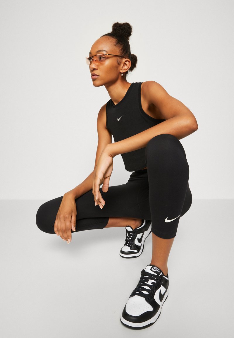 Top crop noir et leggings avec un logo Nike blanc, associés à des sneakers Nike noir et blanc, le tout sur un fond neutre.