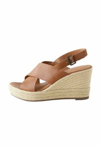 Brown leather wedge sandal with cross strap design, jute-wrapped heel, and adjustable ankle strap, featuring a smooth texture and open toe.