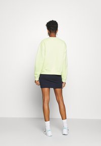 Sweatshirt oversized vert clair à manches longues, associé à une mini-jupe moulante bleu marine, porté avec des chaussures de sport blanches et des chaussettes montantes.