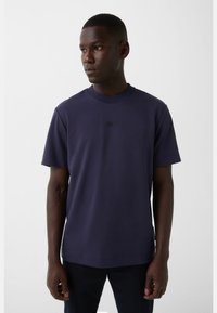 Marineblå crew-neck t-shirt i glat bomuldsblanding med korte ærmer og et diskret logo på brystet, tætsiddende design.