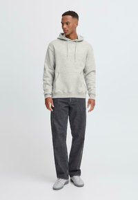 Light gray hoodie with a front pocket and drawstring, paired with dark gray straight-leg jeans and gray sneakers. Plain background.