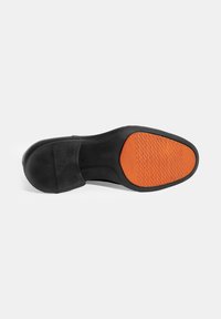 Zwarte schoenzool met een gestructureerde rubberen onderkant. Heeft een oranje accent met een patroon gripgebied. Glad zwart bovenwerk met een ronde neus.