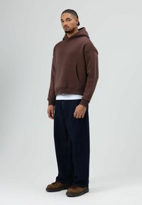 Bruine hoodie met een voorzak, gecombineerd met losse donkerblauwe spijkerbroek en bruine veterschoenen.