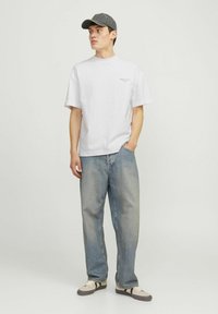 Camiseta de algodón blanca de manga corta y cuello redondo, combinada con jeans de denim azul desgastados. Completada con una gorra gris oscura y zapatos casuales.