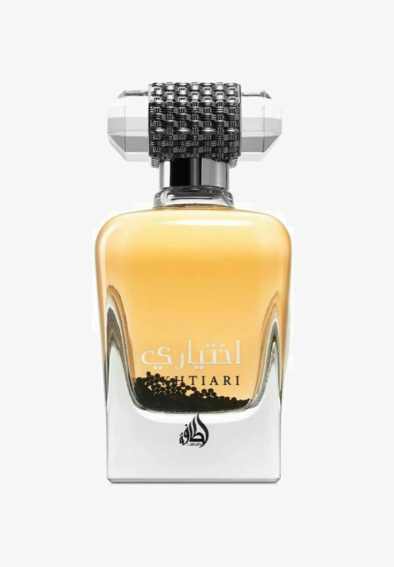 Neliömäinen lasinen hajustepullo, jossa on keltainen neste. Kuusikulmainen musta ja hopea kansi, jossa on teksturoitu pinta ja kirkkaat kristallikoristeet.