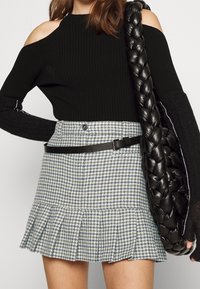 Zwarte geribbelde off-shoulder trui met lange mouwen, gecombineerd met een blauw-witte houndstooth mini-jurk met een gerimpelde zoom en een zwarte riem.