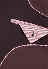 Brązowy materiał z wyraźnym czerwono-białym paskiem na kołnierzu oraz przezroczystym guzikiem. Projekt zawiera zaokrąglone krawędzie i kontrastowe szwy.