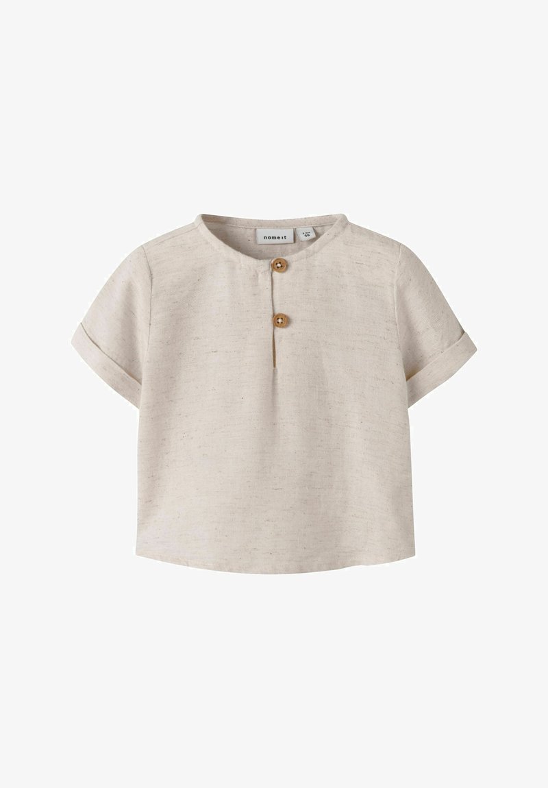 Camiseta beige de manga corta para niño pequeño, con cuello redondo, dos botones de madera en la tapeta frontal y puños de manga remangados.