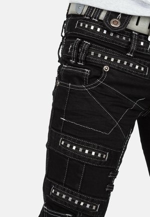 Pantaloni neri con molteplici tasche, cuciture bianche a contrasto e inserti metallici quadrati. Presentano un design patchwork unico e un tessuto resistente.