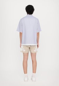 Camicetta a maniche corte, blu chiaro a righe con bordo in pizzo all'orlo, abbinata a pantaloni corti beige con ricami floreali bianchi. Sneakers bianche.