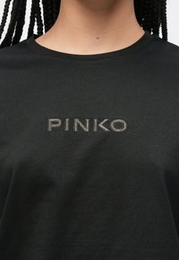 Černé bavlněné tričko s nápisem „PINKO“ z kovových kamínků. Měkký materiál s klasickým kulatým výstřihem.