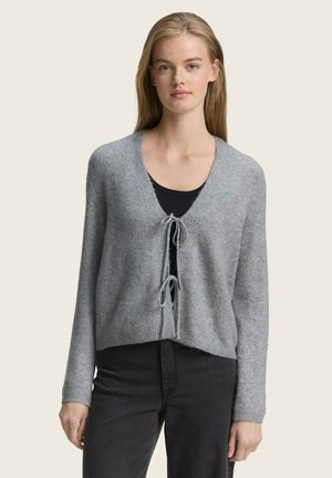 Cardigan gris, court, avec un col en V et fermeture à nouer à l'avant. Texture douce, manches longues et détails en côte à l'ourlet, associé à un top noir.