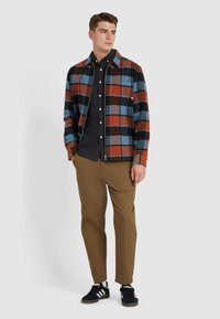 Kariertes Hemd aus orange, blau und schwarz Karst; Knopfdesign mit Kragen. Kombiniert mit beigen Hosen und schwarzen Sneakers.
