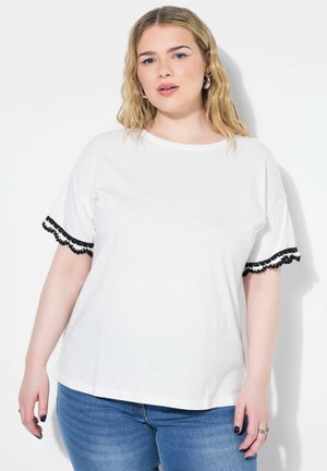 Witte korte mouwen t-shirt met zwarte kanten afwerking op de mouwen. Zachte katoenen stof met een ontspannen pasvorm en een ronde halslijn. Gecombineerd met blauwe jeans.