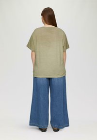 Olive zielenony oversize'owy t-shirt z krótkimi rękawami i okrągłym dekoltem, zestawiony z szerokimi, jasnoniebieskimi dżinsami.