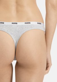 String gris en coton avec une taille blanche arborant le logo "PUMA". Le design est minimal, avec une texture lisse et une taille basse.