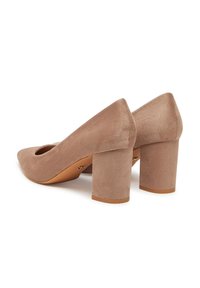Par de zapatos de mujer de ante beige con tacón grueso y punta redondeada, mostrados desde la parte trasera y lateral sobre un fondo blanco.
