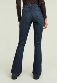 Dark blue flared jeans in denim with a high waistband, two back pockets, and a smooth texture, paired with chunky black platform boots.