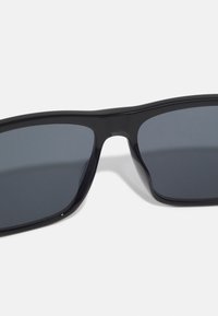 Melni plastmasas saulesbrilles ar taisnstūra rāmi un tumšiem tonētiem stikliem, ar gludu, spīdīgu apdari.