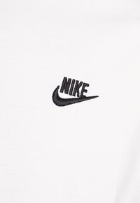 Valge puuvillane T-särk, millel on must tikandiga Nike logo vasakul rinnal, sujuva tekstuuri ja klassikalise ümarakaeluse kujundusega.