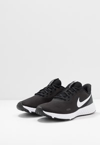 Scarpe sportive nere in mesh con un baffo bianco, punta arrotondata, suola testurizzata e lacci neri, dotate di un'intersuola bianca imbottita.