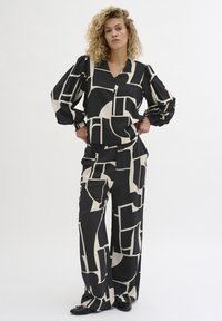 Îmbrăcăminte cu un model geometric în tonuri de negru și crem, care include un top lejer cu mâneci lungi și decolteu în V, împreună cu pantaloni evazați. Textură de țesătură netedă.