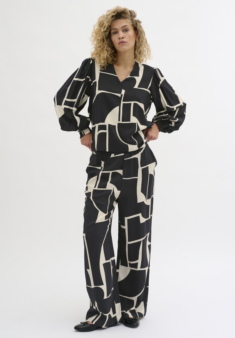 Îmbrăcăminte cu un model geometric în tonuri de negru și crem, care include un top lejer cu mâneci lungi și decolteu în V, împreună cu pantaloni evazați. Textură de țesătură netedă.